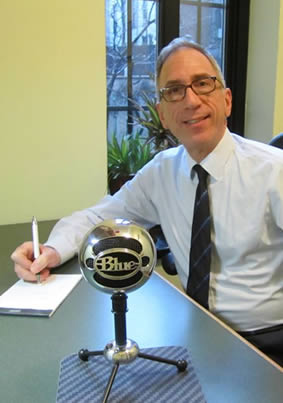 Everett Leiter smiling, holding a pen with a microphone on the table.